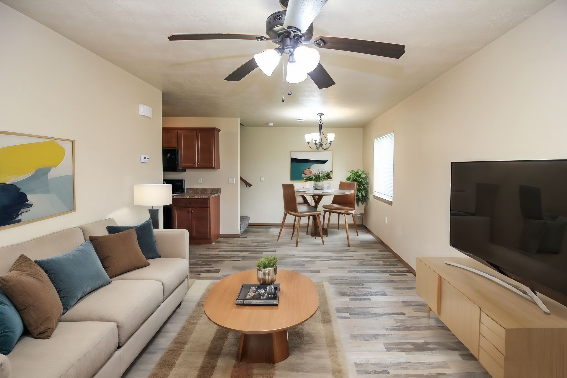Cozy open-plan living room with sofa, coffee table, TV, ceiling fan, and dining area in back