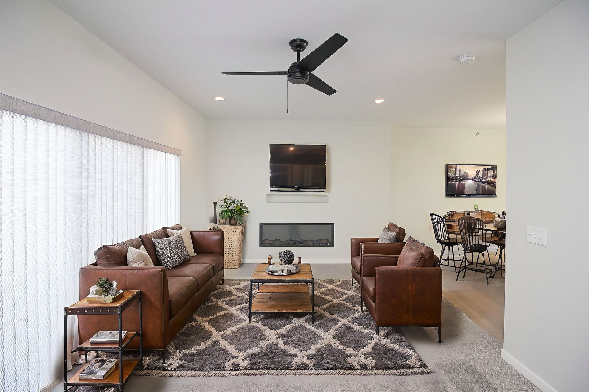 Bright living room with leather sofas, patterned rug, coffee table, ceiling fan, and wall-mounted TV