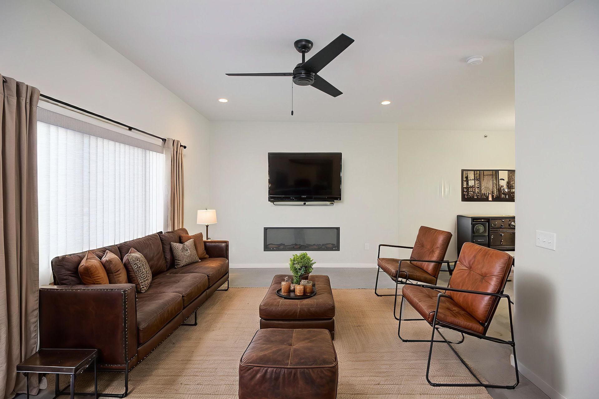 Modern living room with leather sofa, two chairs, wall-mounted TV, and ceiling fan