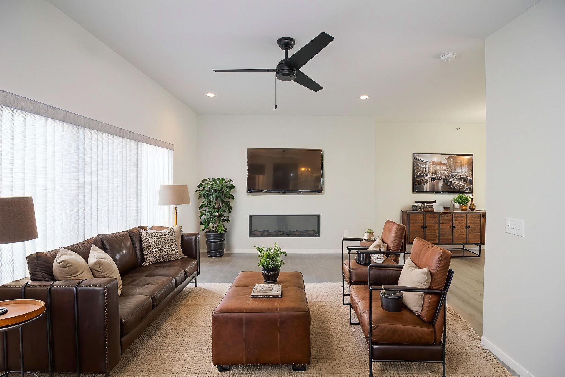 Modern living room with brown leather sofas, coffee table, wall-mounted TV, fireplace, and ceiling fan.