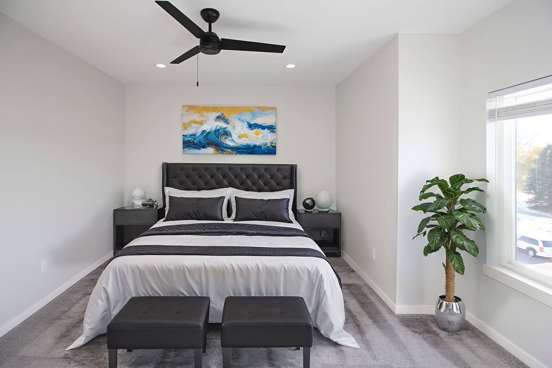 Modern bedroom with a black bed, ceiling fan, wall art, and a large window with a plant.