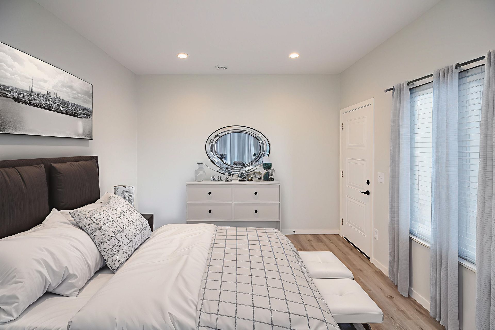 Bright modern bedroom with a bed, dresser, mirror, and sliding glass doors with sheer curtains