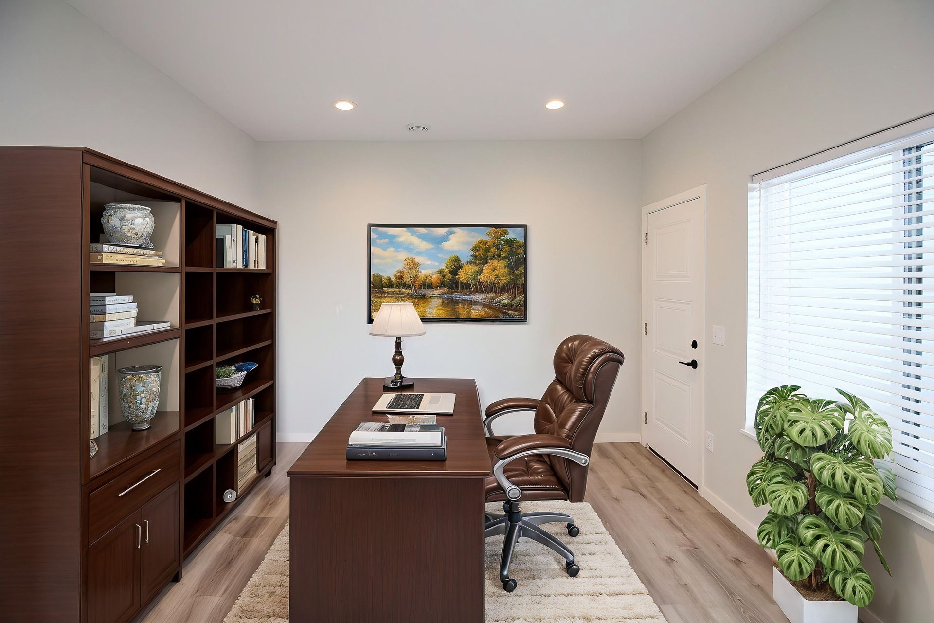 Home office with dark wood desk, bookshelf, chair, and landscape art by a bright window