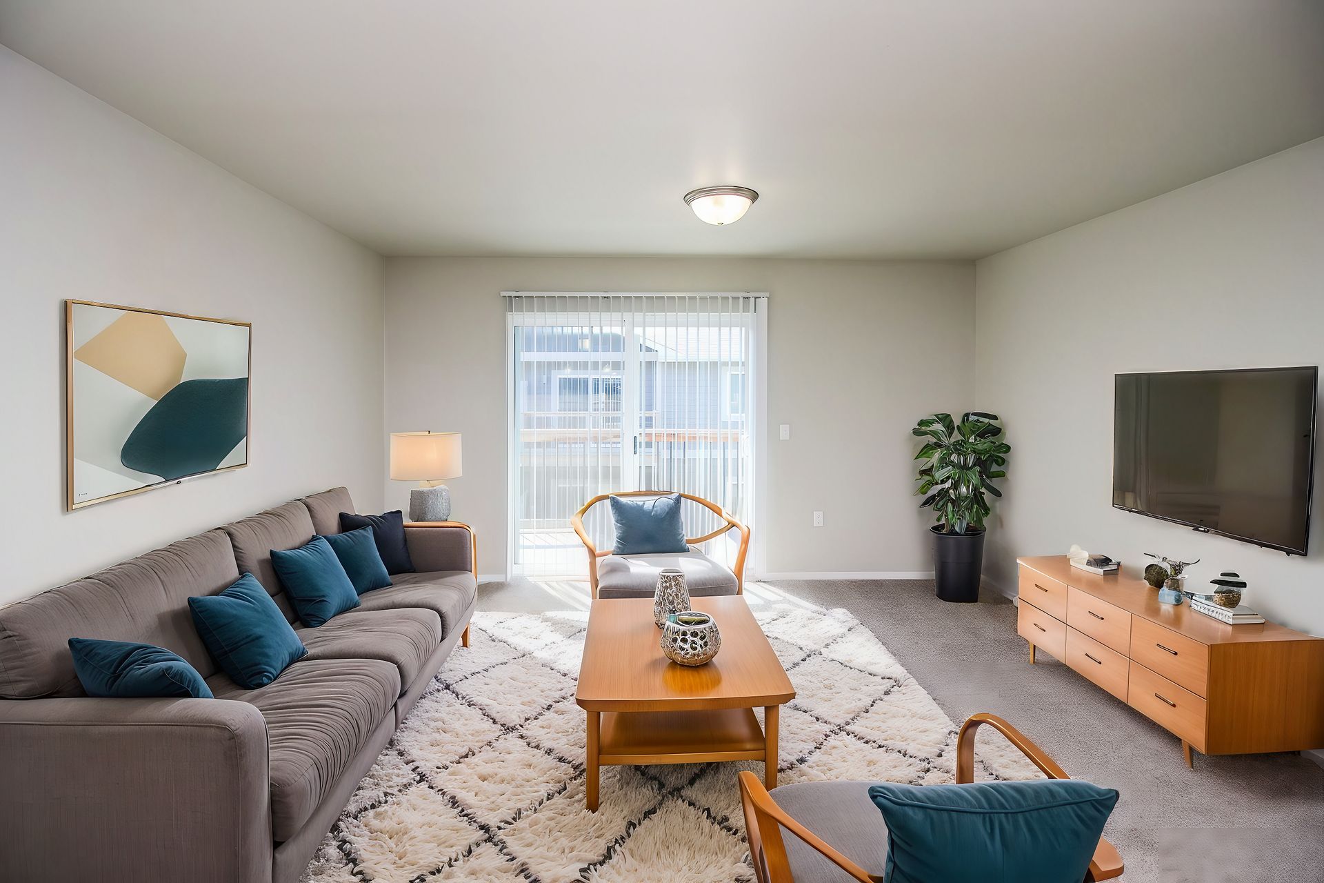 Bright living room with gray sofa, teal chairs, large TV, wooden console, and patterned rug