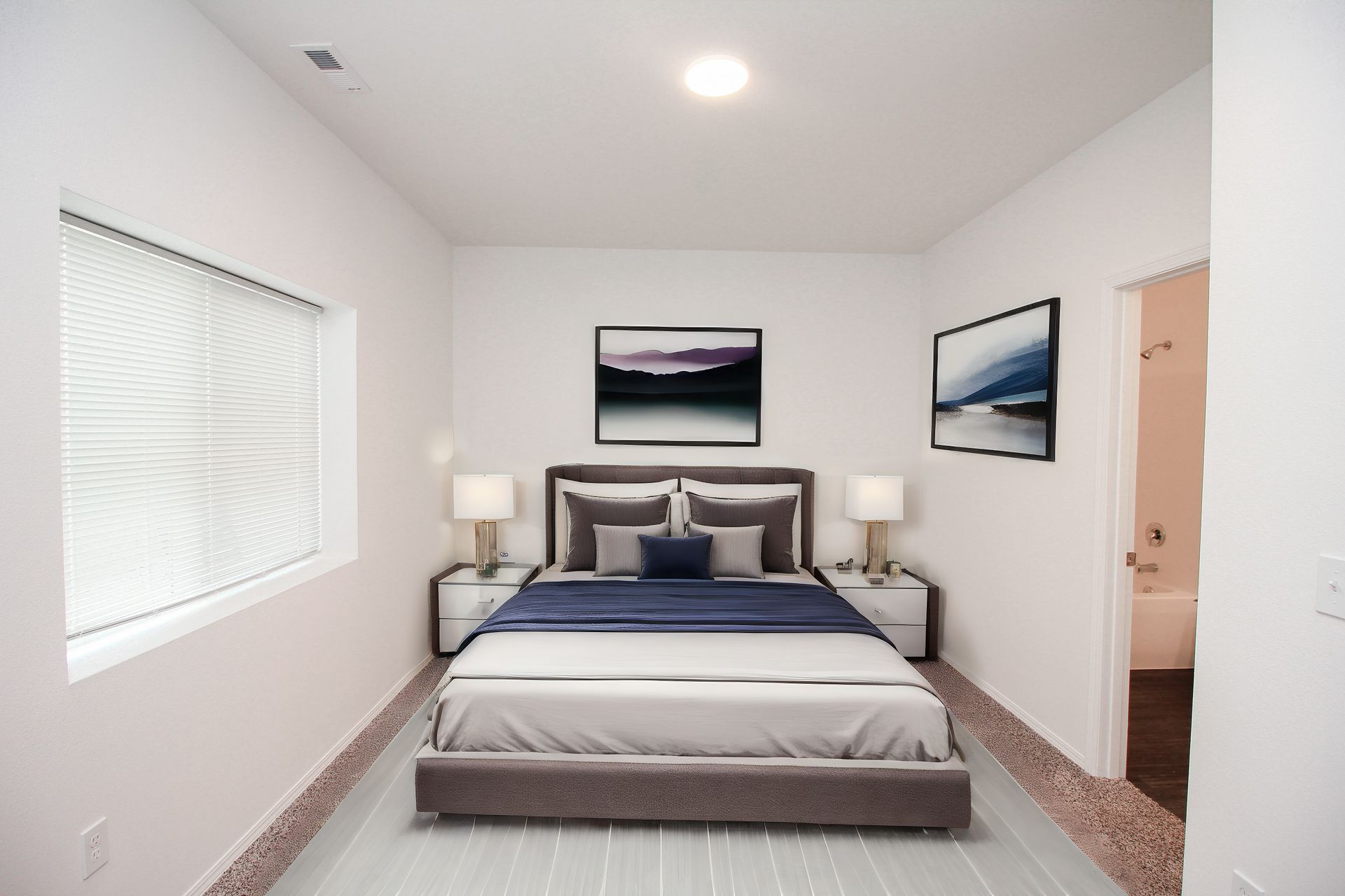 Modern bedroom with a bed, two bedside lamps, framed wall art, and a window with blinds.