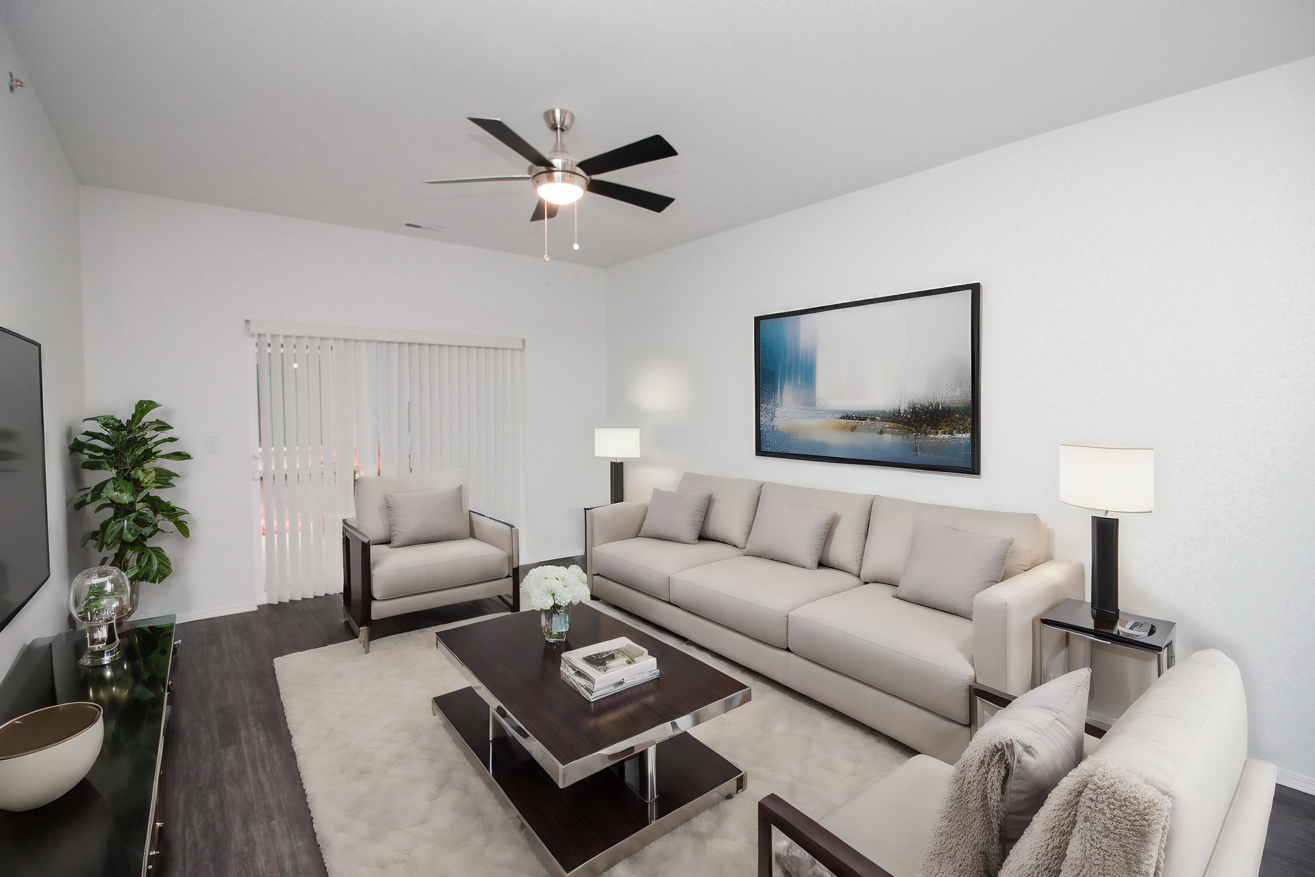 Bright modern living room with gray sofas, coffee table, floor lamps, wall art, and ceiling fan.