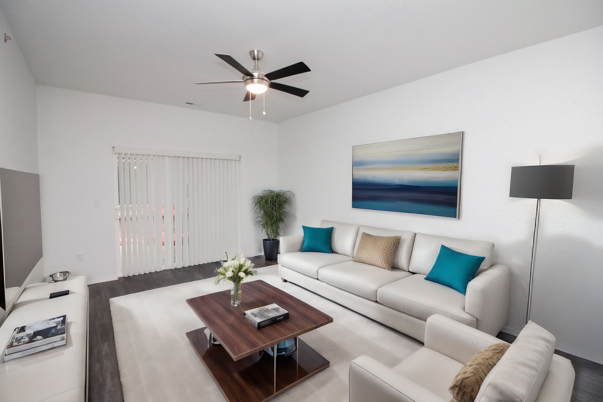 Bright modern living room with white sofa, dark coffee table, ceiling fan, and blue wall art