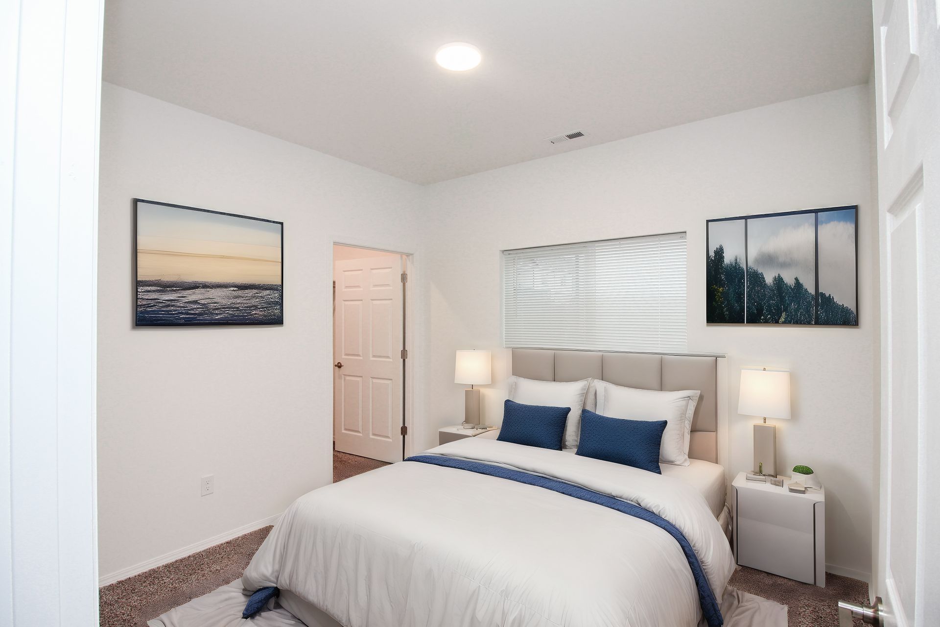 Bright white bedroom with a neatly made bed, bedside lamps, and framed wall art.