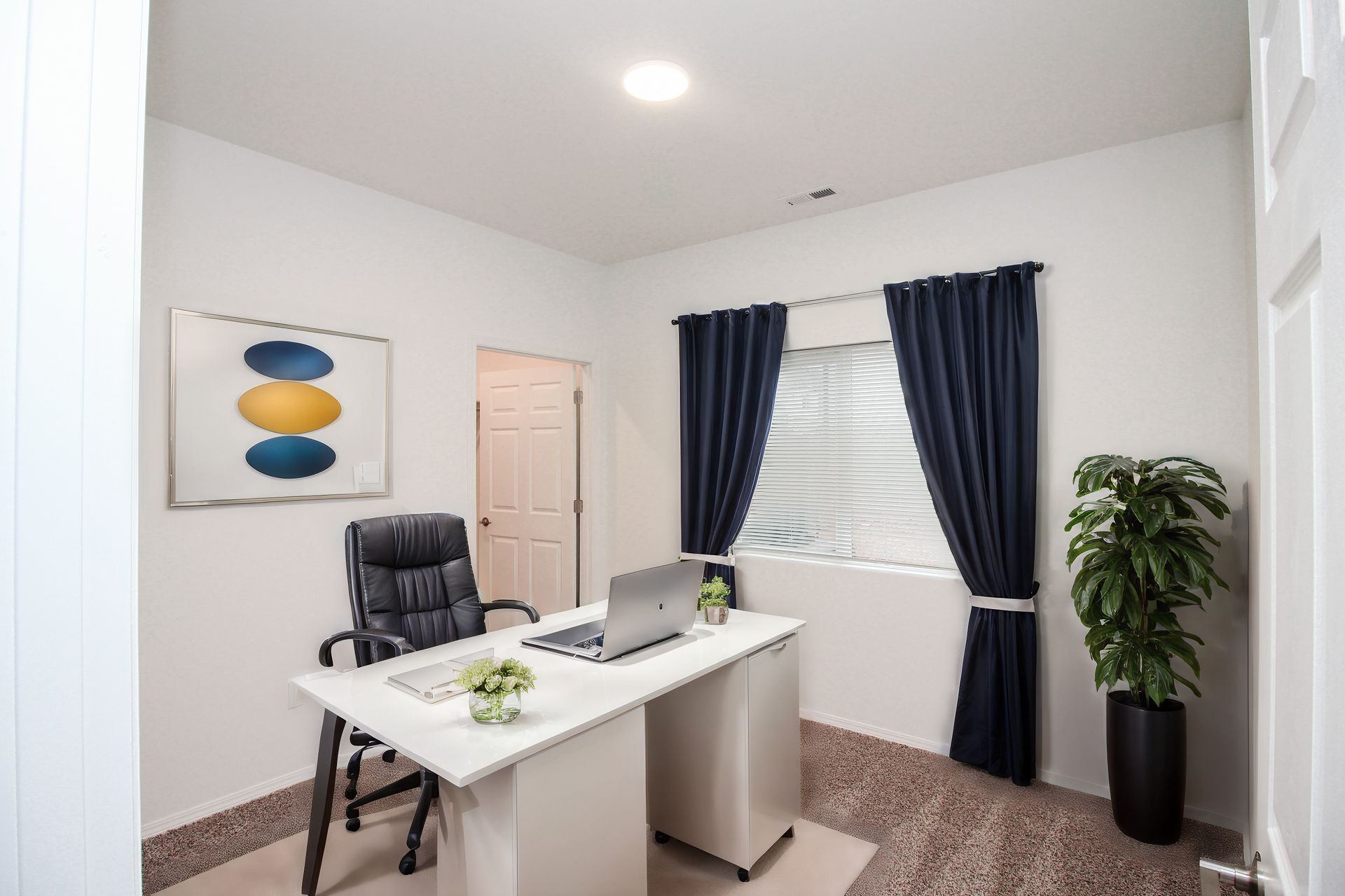 Modern home office with white desk, black chair, laptop, dark curtains, and potted plant.