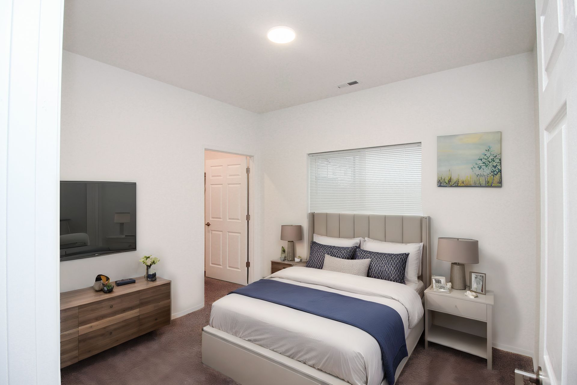 Bright white bedroom with a bed, dresser, nightstand, wall art, and window blinds