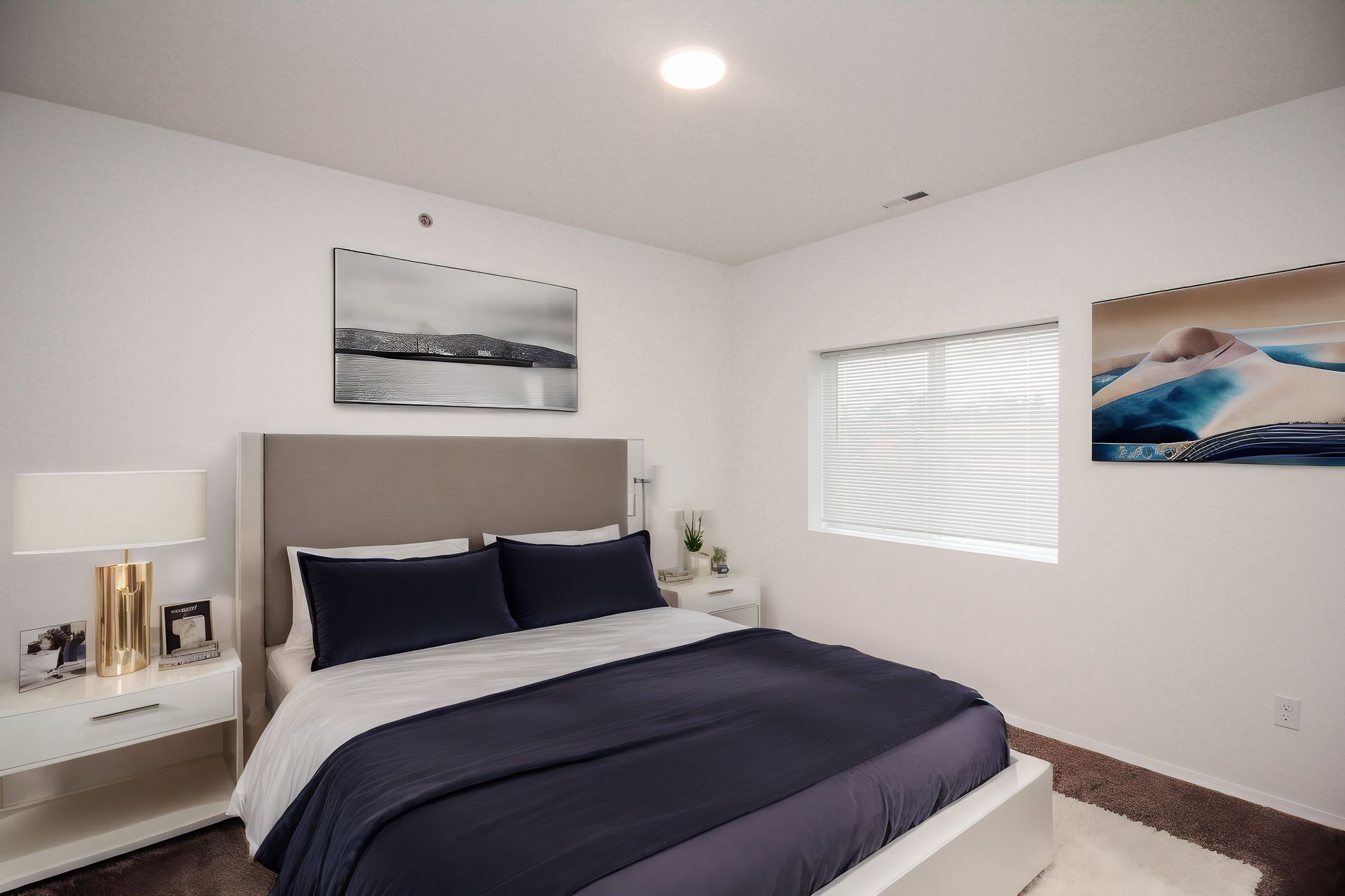 Modern bedroom with bed, navy bedding, nightstand lamp, and wall art by a bright window