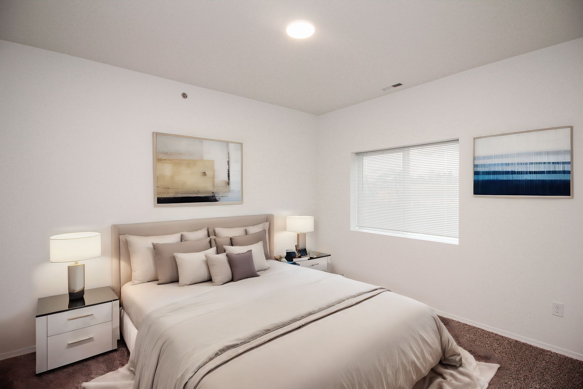Bright bedroom with a made bed, bedside lamps, white walls, and a window with blinds.