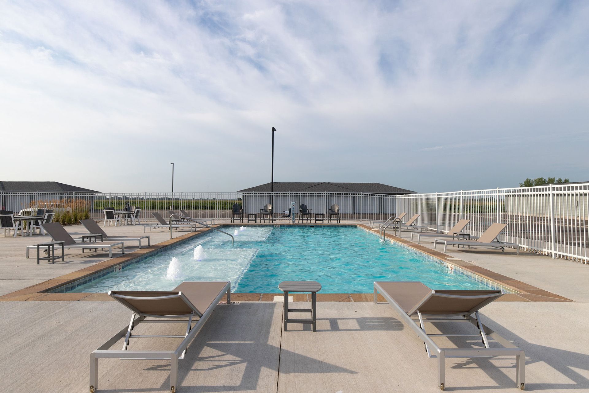 Outdoor swimming pool with lounge chairs and white fence under a cloudy sky