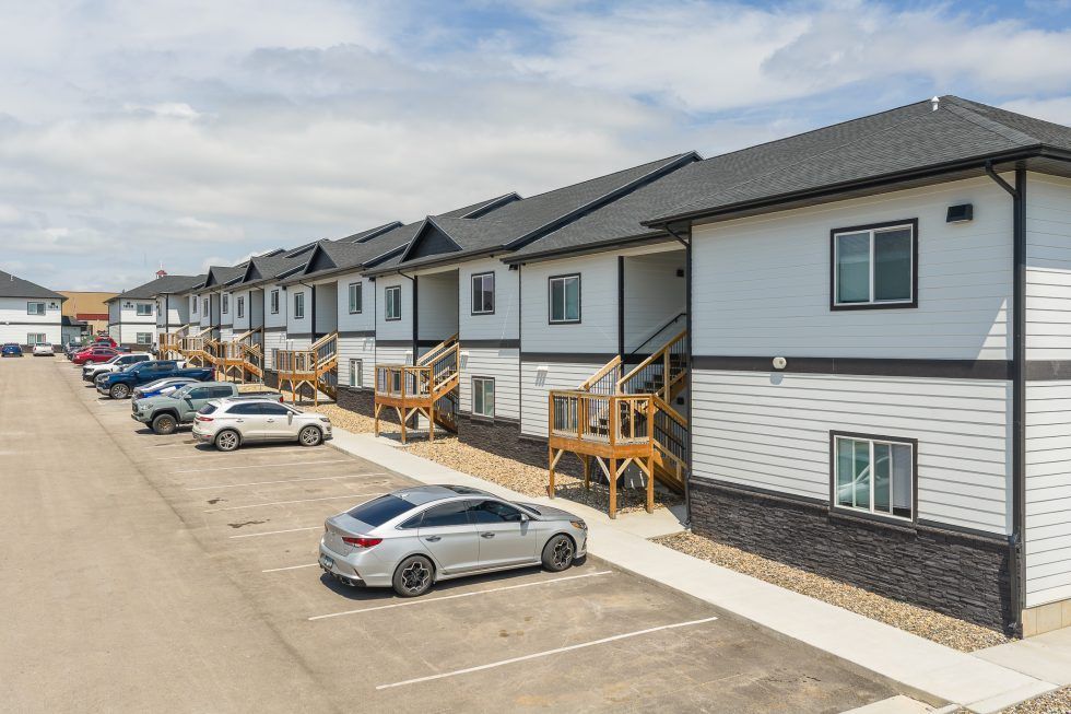 Row of modern gray townhomes with parked cars along a paved street under a cloudy sky