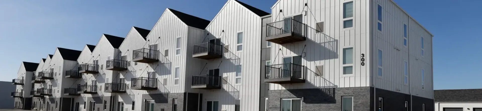 Modern white apartment buildings with balconies and sharp rooflines on a sunny street