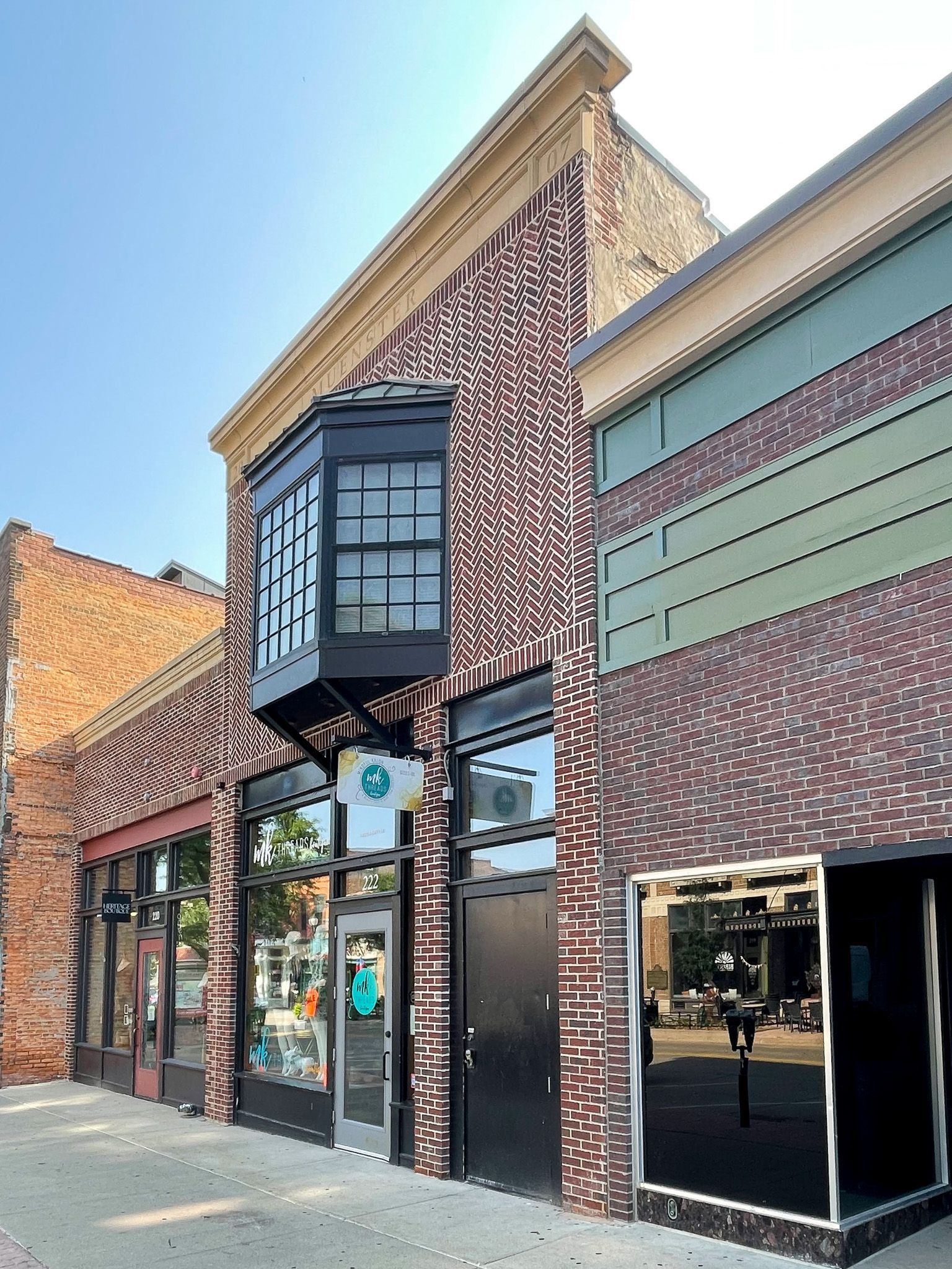 Brick storefront with large windows and decorative metal trim on a sunny street.