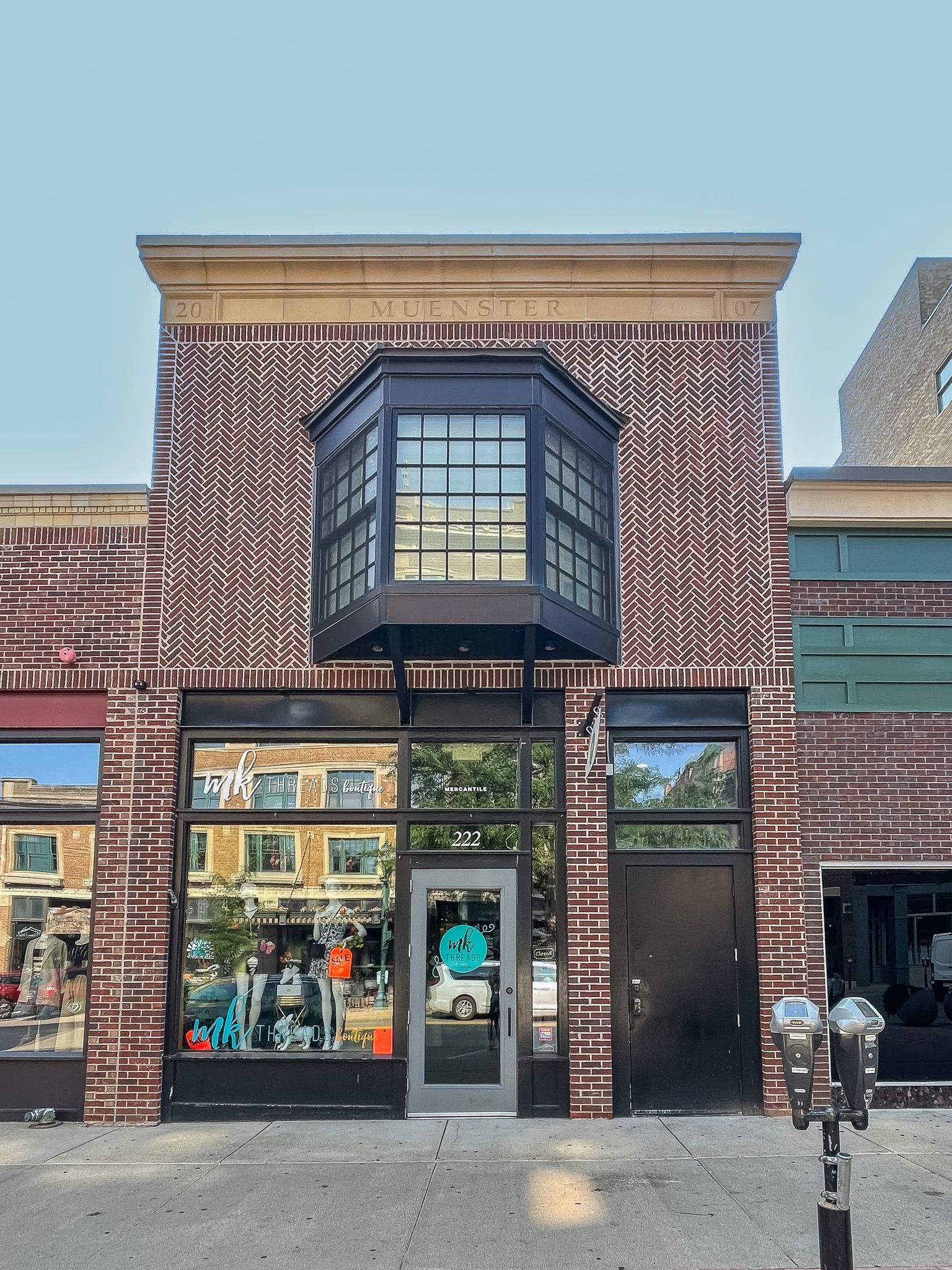 Historic brick storefront with patterned facade, large windows, and a central bay window on a sunny street.