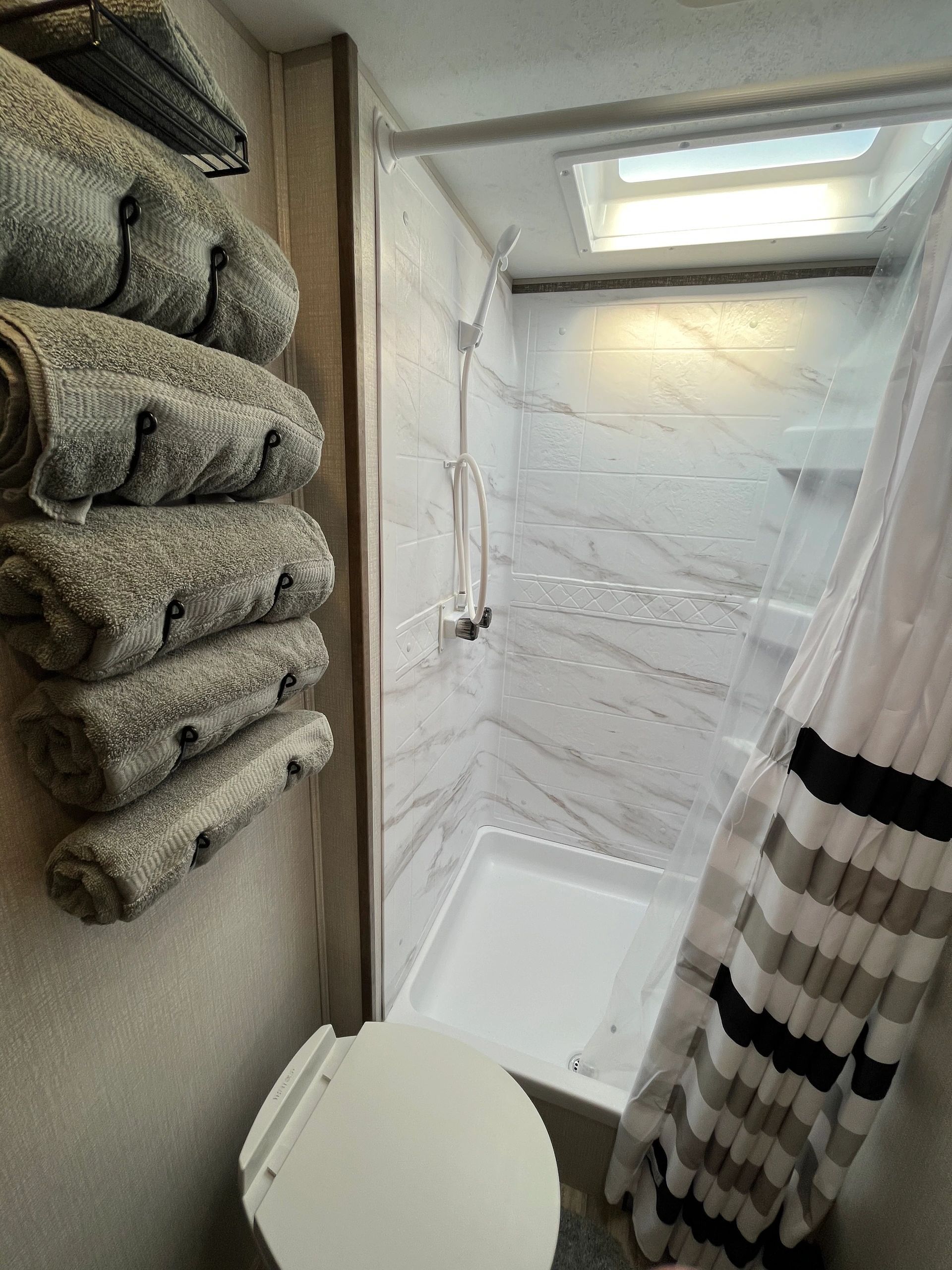 A bathroom with a toilet , shower and a stack of towels.