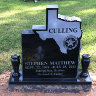A black granite headstone shaped like Texas, engraved with 
