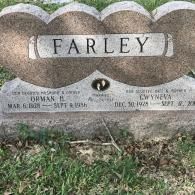 A gray stone double-heart headstone for Orman B. and Gwyneva Farley, showing birth and death dates on a grassy background.