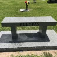 A gray granite cemetery bench with 