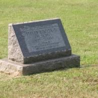 A dark grey granite headstone with inscribed text, set in a grassy field.