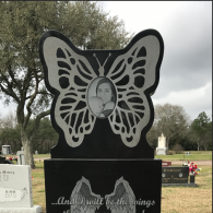 A black granite gravestone shaped like a butterfly with a central portrait, engraved with angel wings and text.