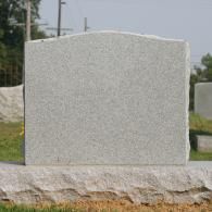 A blank, gray granite headstone set on a natural rock base in a cemetery.