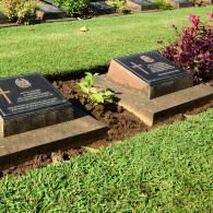 Two black granite grave markers set in a grassy cemetery plot, with a small bush nearby.