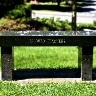 A black granite memorial bench sits on a grassy lawn with the inscription 