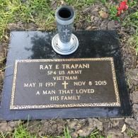 A bronze grave marker for Ray E. Trapani, a Vietnam veteran, set in a black stone base with a flower vase on top.