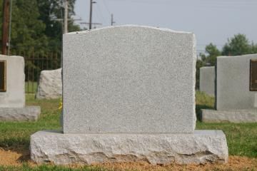 A light gray, granite headstone with a curved top stands in a cemetery on a grassy lawn.
