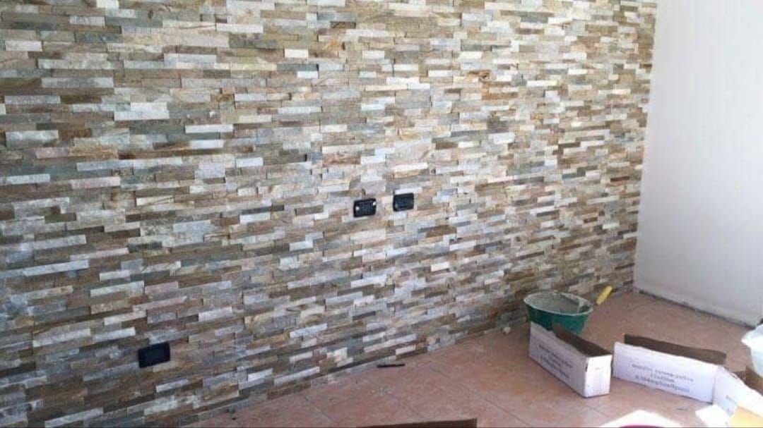 Una parete rivestita di piastrelle di pietra irregolari, multicolori e dalla superficie ruvida, con tre prese elettriche a vista.