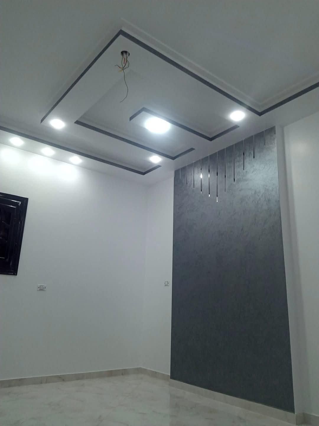 Interno di una stanza moderna caratterizzato da una parete decorativa grigia con texture, un soffitto a cassettoni quadrati con illuminazione a LED e pavimenti piastrellati.