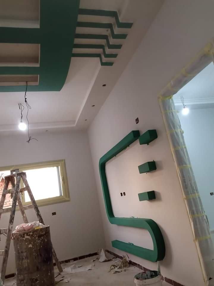Una stanza in fase di ristrutturazione con un soffitto decorato con motivi geometrici verdi e una parete decorativa a forma di S, anch'essa verde, abbinata.