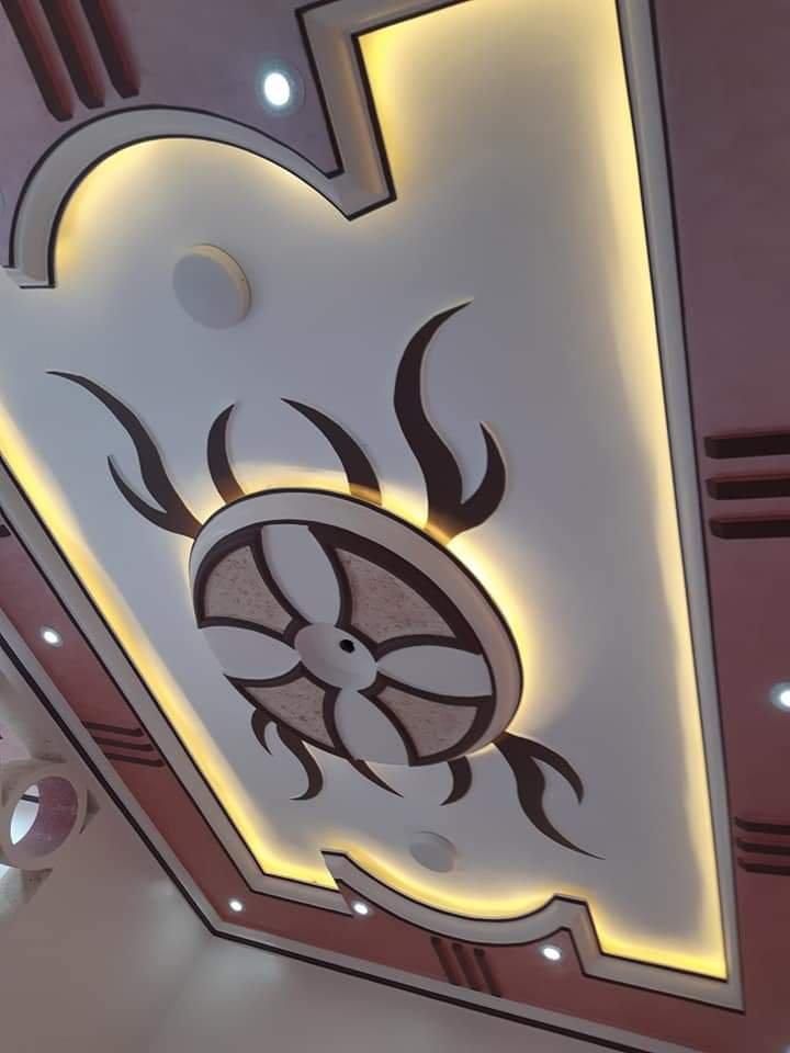 Un soffitto moderno caratterizzato da un motivo floreale centrale, illuminazione ambientale a incasso dorata e finiture geometriche marroni e bianche.