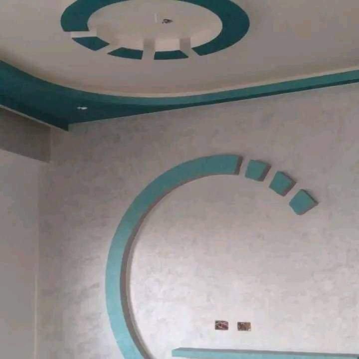 Interno di una stanza caratterizzato da un soffitto con un elemento decorativo circolare color verde acqua e da un motivo a mezzaluna abbinato su una parete bianca.