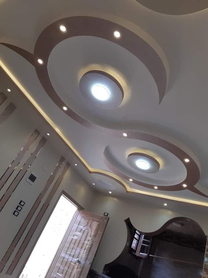 Un soffitto moderno con un design curvilineo a due tonalità, crema e marrone, con incavi e illuminazione circolare integrata.