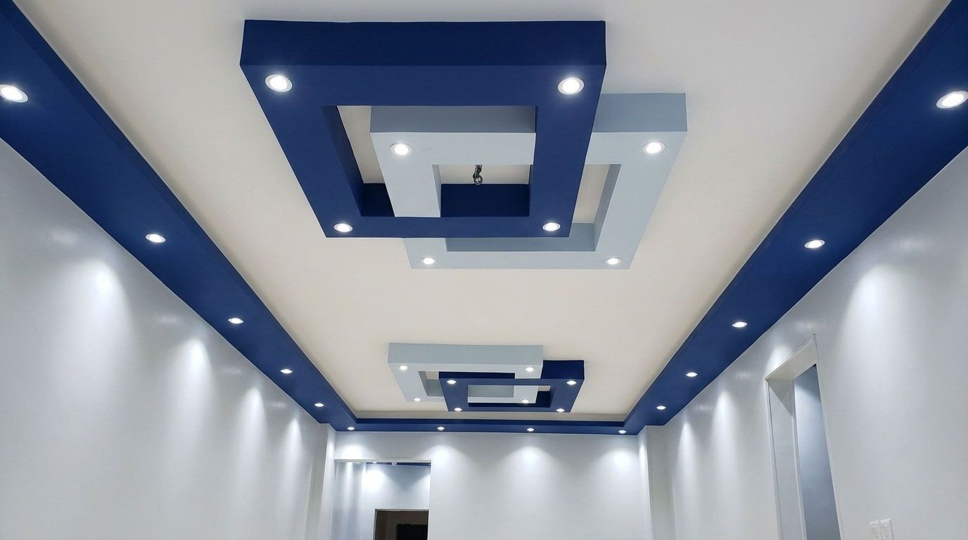 Soffitto moderno con pannelli geometrici incassati nei toni del blu e del grigio chiaro, illuminato da una delicata luce a incasso e perimetrale.