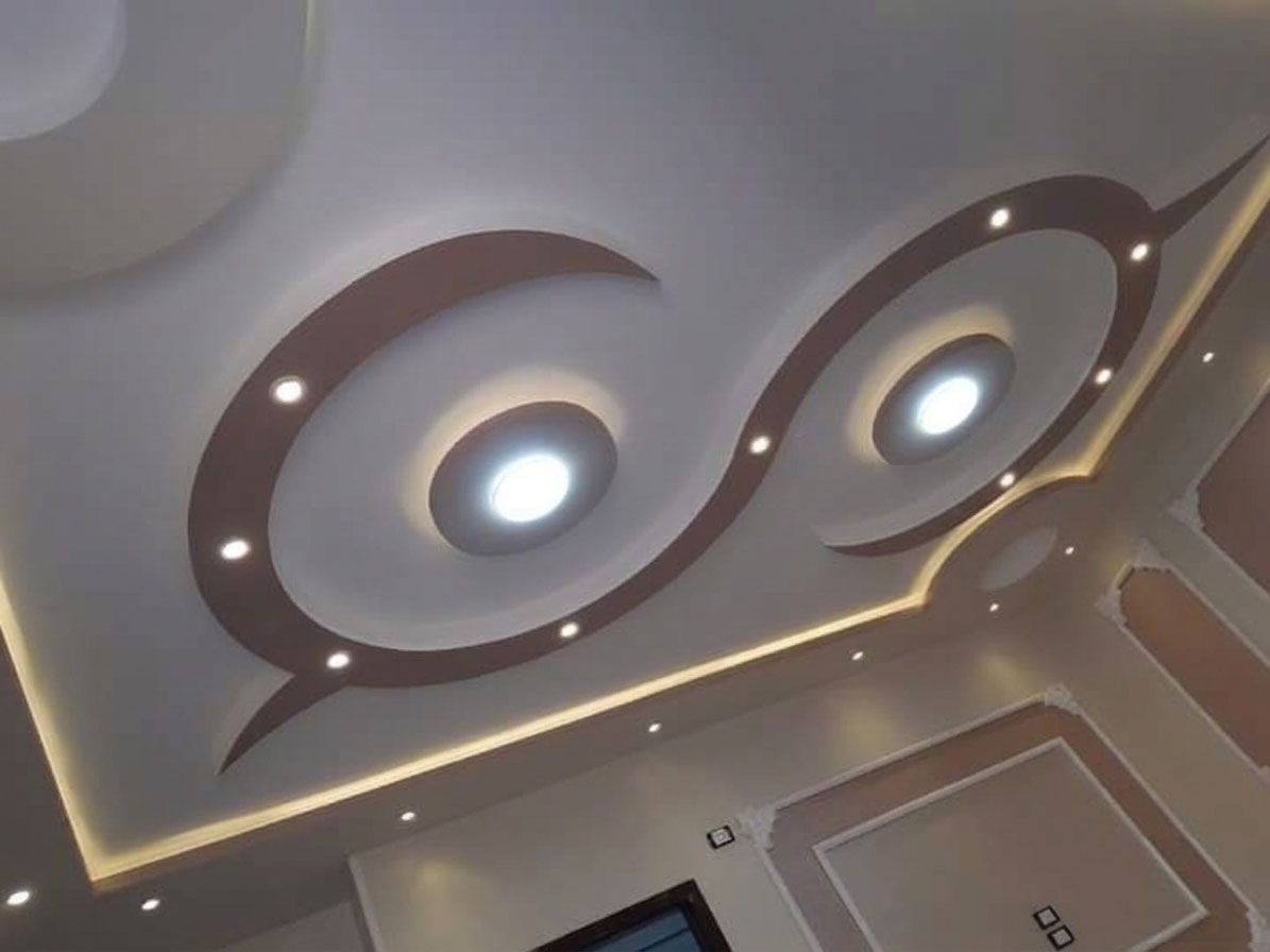 Un controsoffitto moderno caratterizzato da un design a S di colore marrone con faretti a incasso e illuminazione ambientale perimetrale.