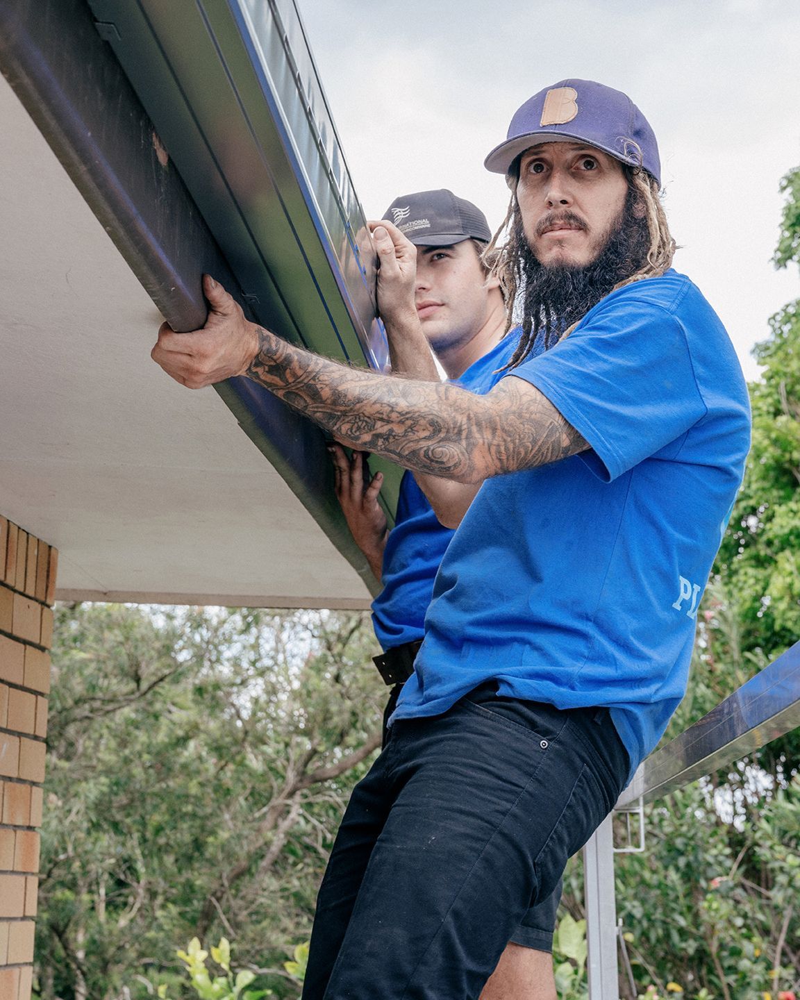 Two men are working on a gutter on the side of a house in Coffs Harbour.