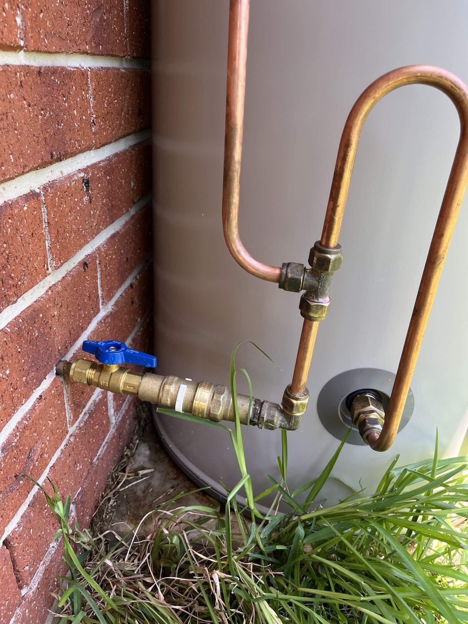 A water heater with copper pipes attached to it is sitting next to a brick wall.