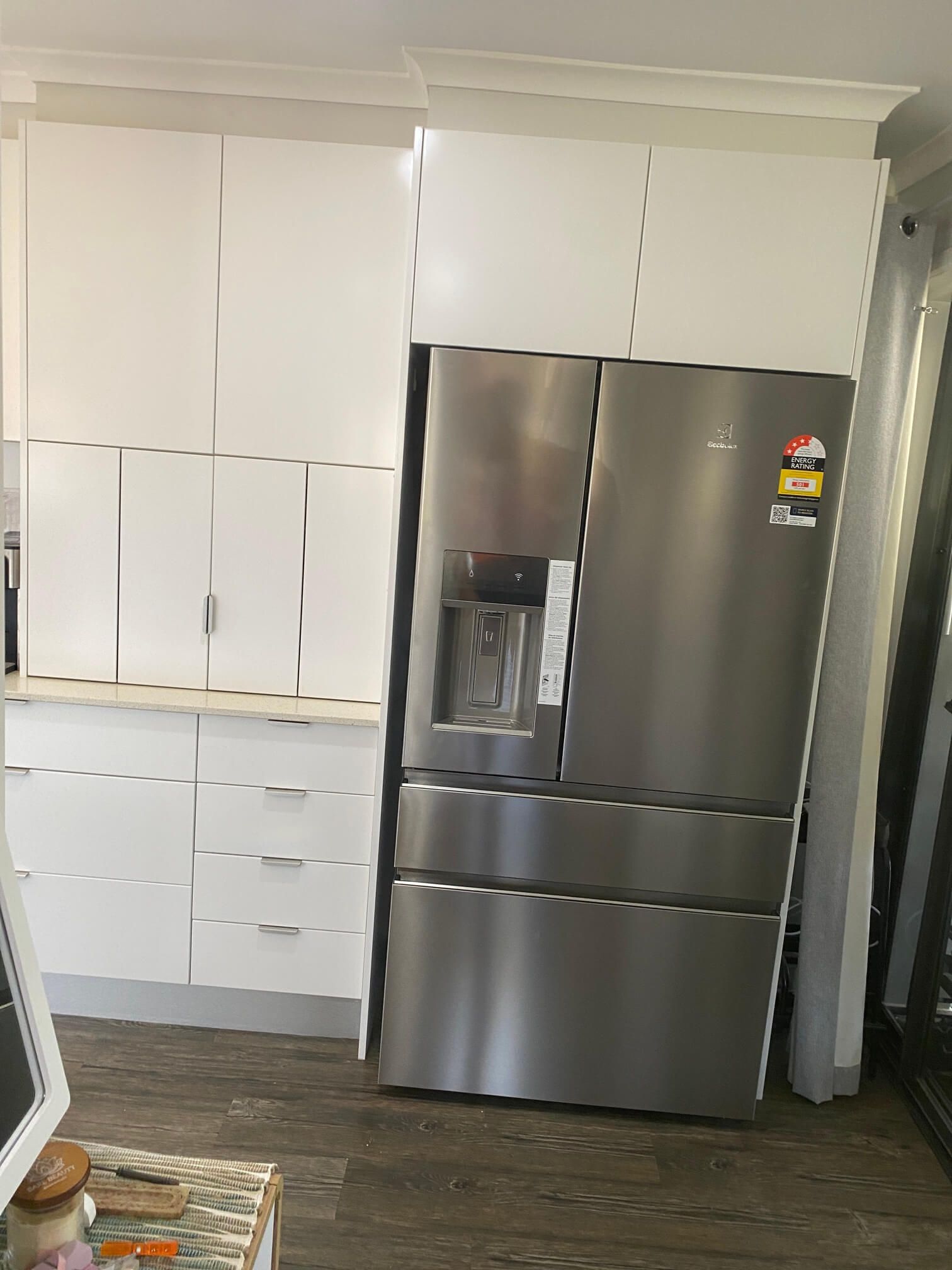 A stainless steel refrigerator sits next to white kitchen cabinetry with upper and lower storage.