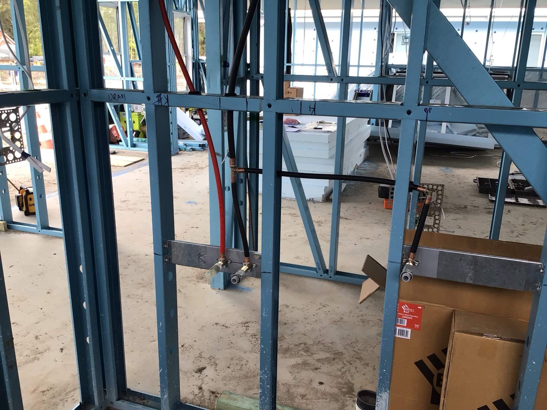 Metal wall framing under construction with exposed red and black plumbing pipes secured to mounting plates.