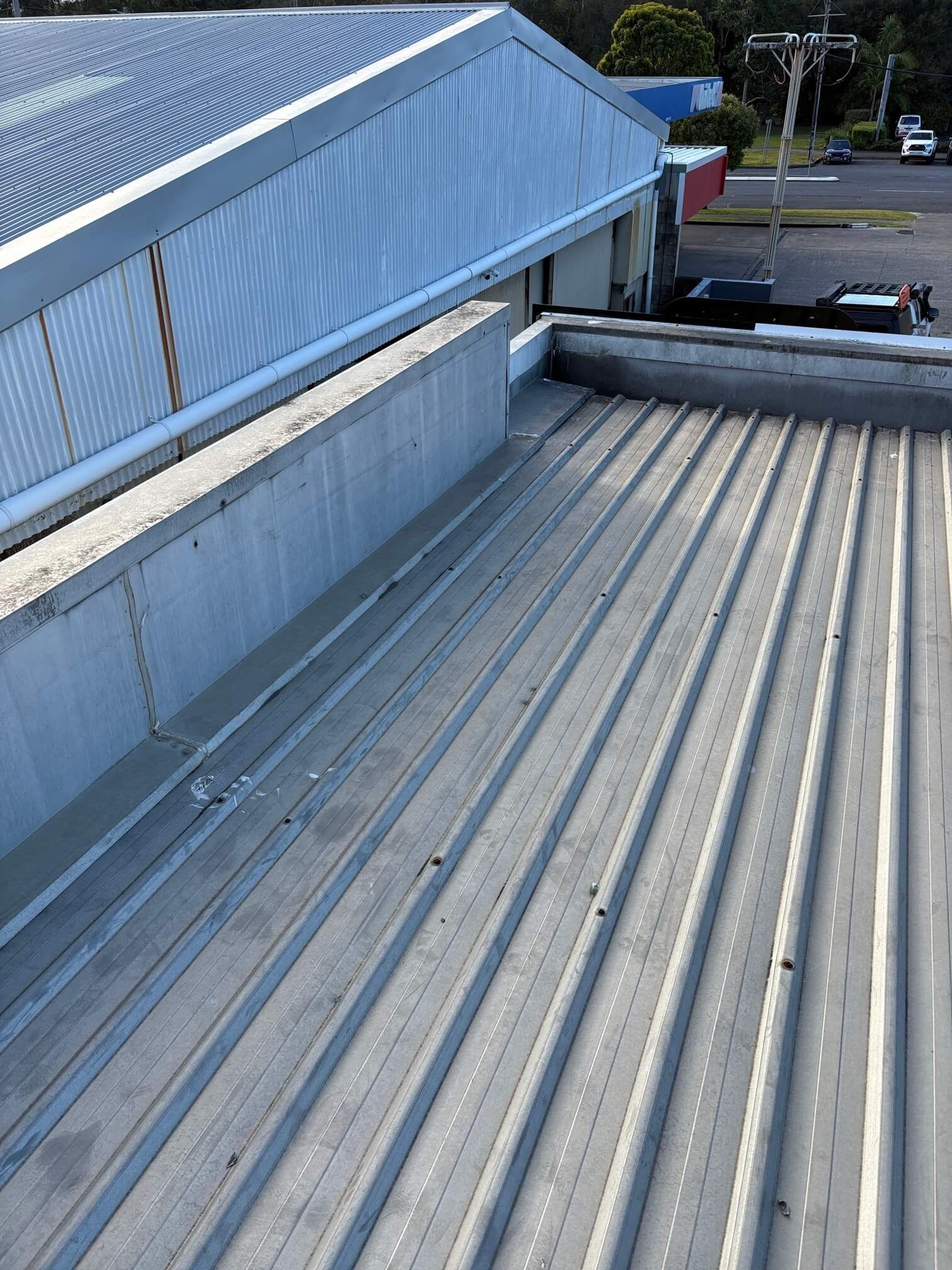 High-angle view of a metal corrugated roof section adjacent to a concrete parapet wall and a larger building structure.