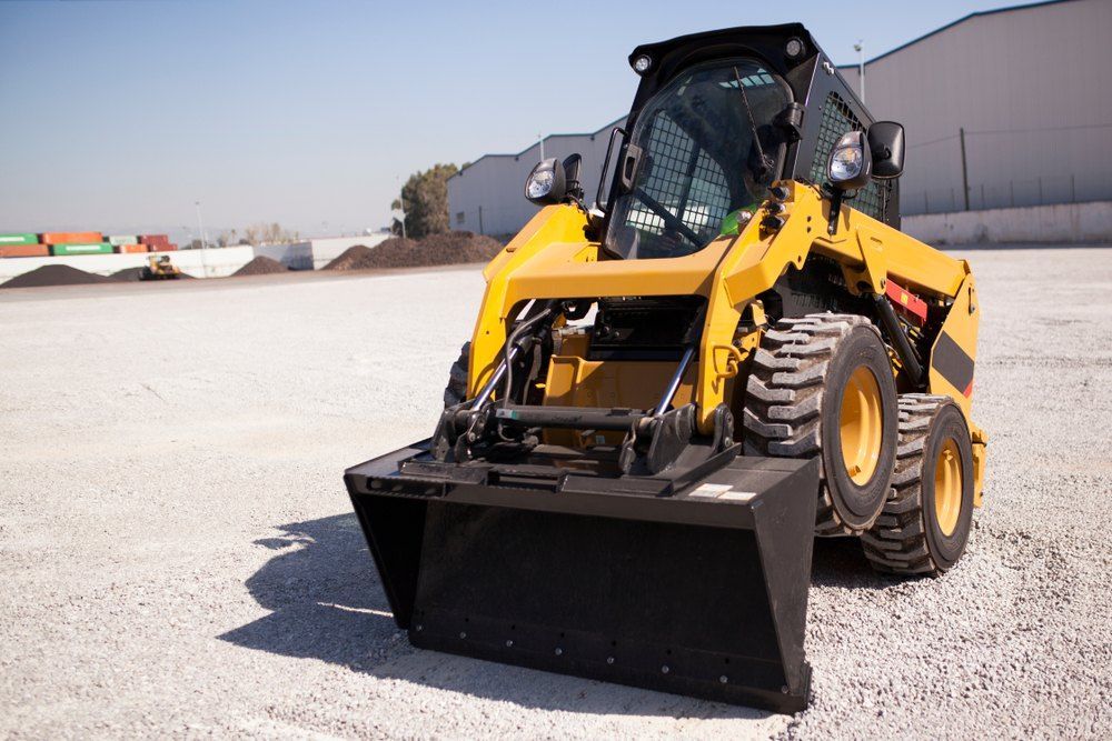 A Yellow Tractor With a Black Bucket is Parked in a Parking Lot — Bennettron Demex in Byron Bay, NSW