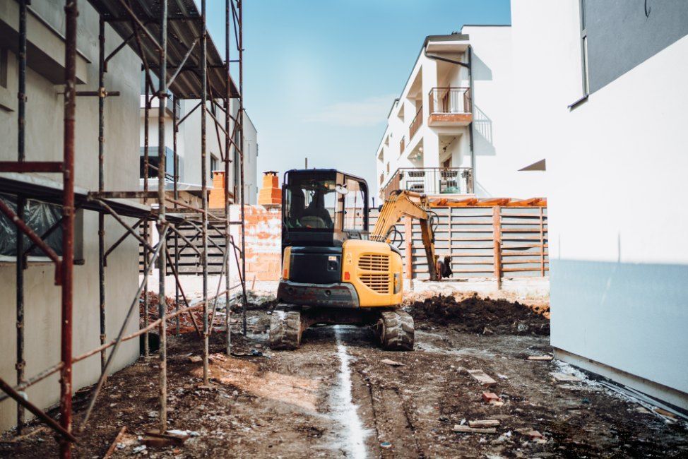 A Yellow Excavator is Driving Down a Dirt Road in Front of a Building Under Construction — Bennettron Demex in Gunnedah, NSW