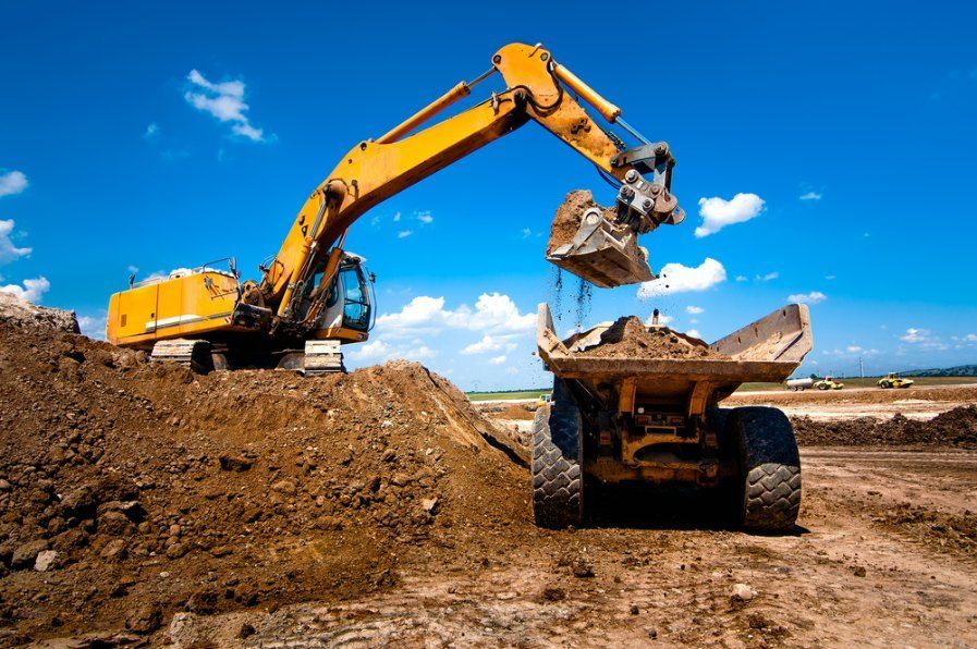 A yellow excavator is loading dirt into a dump truck — Bennettron Demex in Corindi Beach, NSW