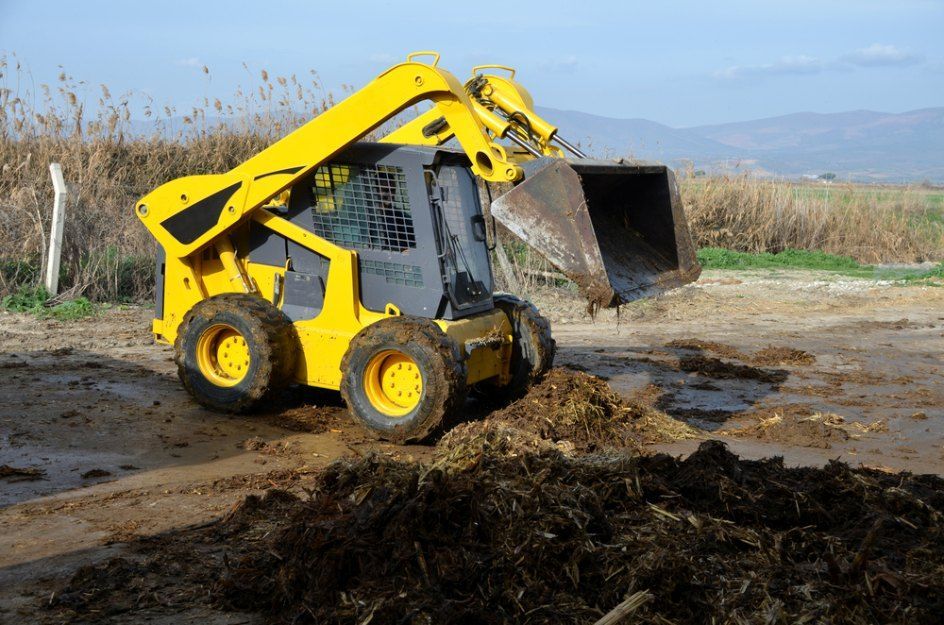 A Yellow Skid Steer is Loading Dirt Into a Bucket — Bennettron Demex in Bonville, NSW