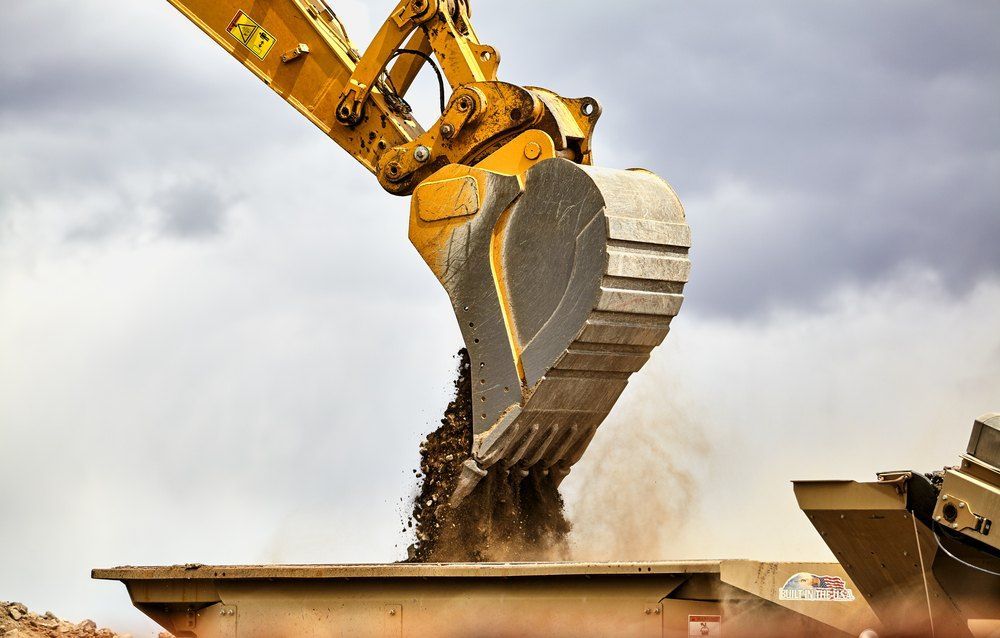 A yellow excavator is scooping dirt into a dumpster — Bennettron Demex in Corindi Beach, NSW